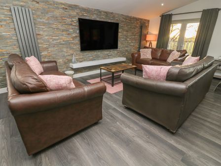 A living room with three brown leather sofas a wall-mounted flat screen television and a coffee table at Box Tree Escapes Wennington near Kirkby Lonsdale