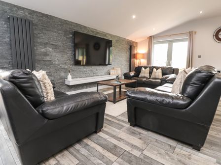 A living room with black leather sofas a wooden coffee table a wall-mounted flat screen television and a stone accent wall at Box Tree Escapes in Wennington near Kirkby Lonsdale