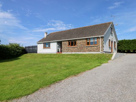 A single-story house with a tiled roof stone and white walls with a lawn and gravel driveway at Oakland Cottage in Summerhill near Saundersfoot