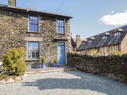 Stone house with blue door and windows with shutters next to stone wall and gravel yard at Hazelnut Cottage in Windermere