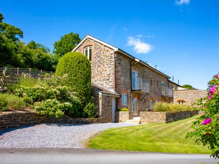 A stone house with balconies and a gravel driveway surrounded by greenery at Maristow Cottage in Cornworthy