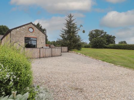 A stone house with a gravel driveway and wooden fences next to a grassy field at The Old Workshop in Denbigh