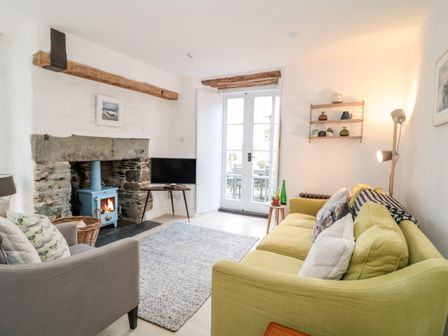 A living room with a green sofa a gray armchair a blue wood stove and French doors at 1 Jubilee Cottage in Trebarwith Strand