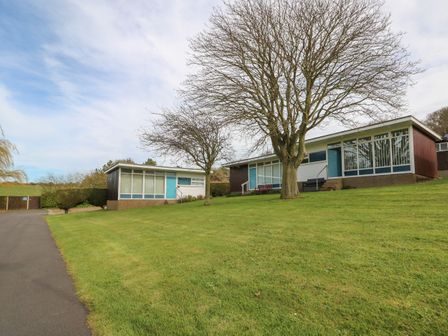 A grassy area with two single-story buildings and leafless trees at Pebbles in Cromer