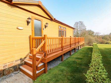 A wooden house exterior with stairs and a railing leading to a door and a lawn with a hedge at Jules @ 79 in Stepaside