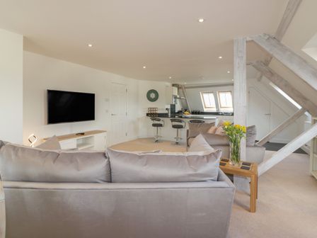 A living area with two sofas a wall-mounted TV and an open kitchen with bar stools at Stores & Supplies in Bodmin