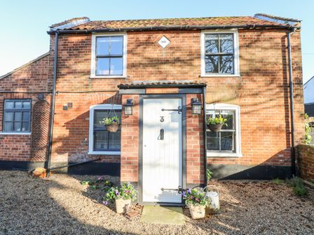 A brick cottage with a white door numbered 3 and hanging flower baskets at Foundry Cottage in Reedham