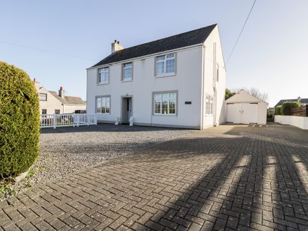 A two story white house with a paved driveway and a detached garage at Halcyon Moelfre near Benllech
