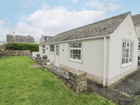 A single-story detached building with windows and a door surrounded by a stone wall and green grass at Halcyon Annexe in Moelfre near Benllech