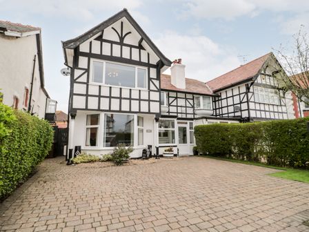 A driveway with brick paving leading to a black and white Tudor-style house with hedges on both sides at Glendalough in Rhos-On-Sea