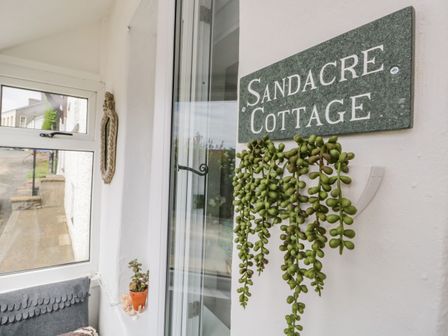 A porch area with a glass door a green hanging plant and a sign that reads Sandacre Cottage at Bardsea