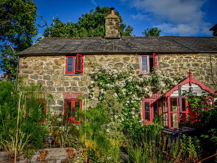A stone cottage with red windows and a garden with plants and flowers at Bwthyn Dyfi in Cemmaes