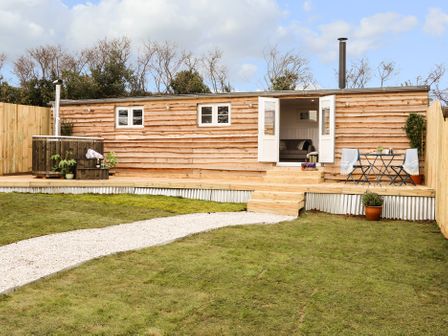 A wooden cabin with open doors a small deck and a wooden hot tub with plants on the deck at Sebright in St Austell