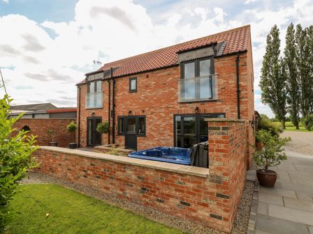 A two-story brick house with glass doors and balconies and a blue hot tub in a walled yard at The Old Doghouse in Sutton-on-the Forest near Huby