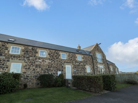 A stone house with white windows and doors surrounded by grass and shrubs at Low Croft in Embleton