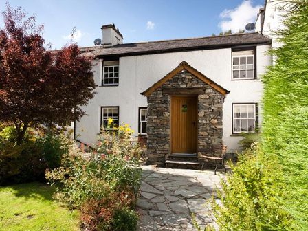 Stone house with wooden door surrounded by garden and trees at Bobbin Beck Cottage in Satterthwaite