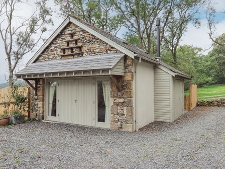 A stone and wood building with closed double doors and windows on a gravel driveway at Dove Tail Barn in Kendal