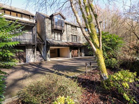 A stone house with garages and stairs surrounded by trees and shrubs at Spring Cottage in Ambleside