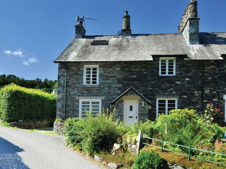 A stone cottage with white framed windows and a garden in front at River Bank Langdale