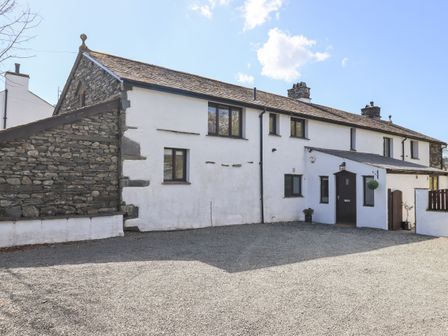 The exterior of a white stone house with multiple windows and a dark door with gravel in front at Ecclerigg Garth in Troutbeck