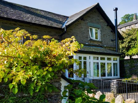 A stone cottage with white framed windows and a garden with green and yellow foliage at Applethwaite Cottage in Troutbeck near Windermere