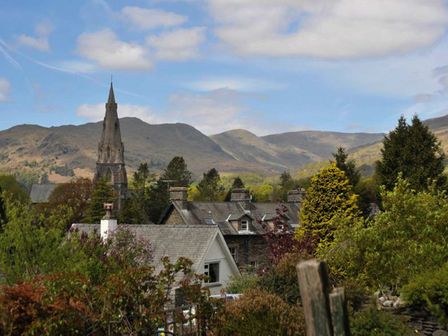 A village with houses and a church tower with mountains and trees in the background at Uldale in Ambleside