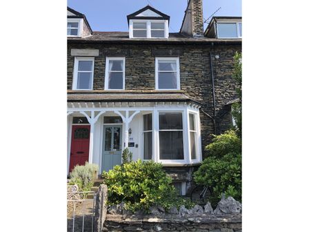 Stone terraced house with bay window blue front door and garden bushes at Highbank in Bowness