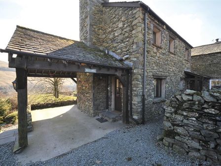 Exterior view of a stone cottage with a wooden porch and gravel pathway at Butt Hill Cottage in Troutbeck