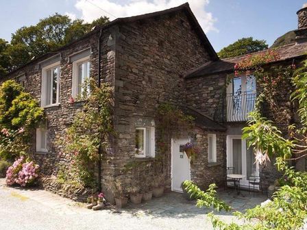 Exterior view of a stone house with white doors and windows and plants growing around at Hart Head Barn in Rydal