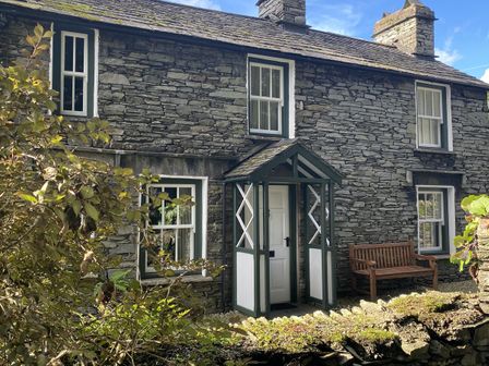 Stone cottage exterior with white door porch wooden bench and surrounding plants at Dove Holme Cottage in Grasmere
