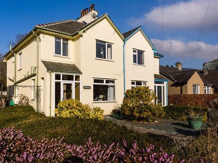 A semi detached cream colored house with shrubs and flowers in the front garden at Heathfield in Keswick