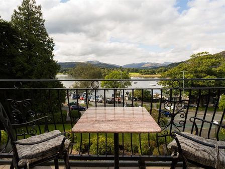 A balcony with a table and two chairs overlooking a parking lot river and mountains at Pure Grace in Ambleside