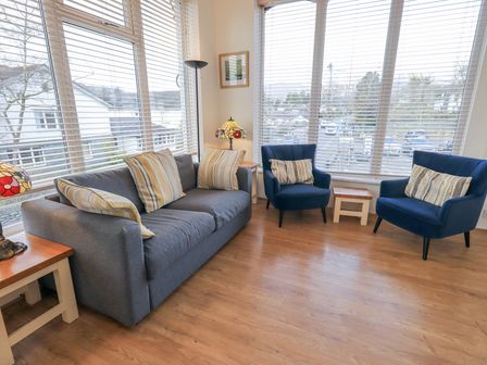 A sitting area with a gray sofa and two blue chairs with striped cushions near large windows at Windows in Ambleside
