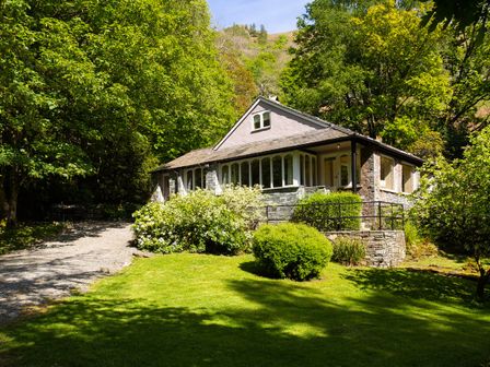A house with stone walls and large windows surrounded by trees and bushes at Underheron in Grasmere