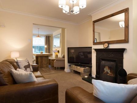 A living room with leather sofas a fireplace and a television with a dining area visible beyond at Noble Cottage in Keswick