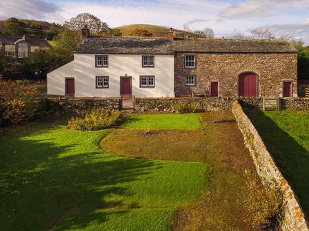 A farmhouse with a stone wall and green lawn in front at Low Longthwaite Farm in Ullswater