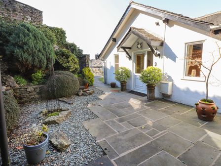 A stone patio with potted plants and a white door on a house exterior at Courtyard Cottage in Ambleside