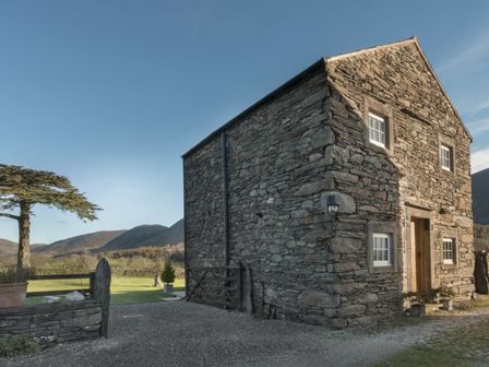 A stone house with small windows and a wooden door next to a tree and grassy area at Cedar Nook in Loweswater