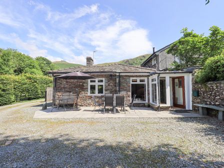 A stone cottage with outdoor patio furniture and an umbrella in a rural setting at Rowan Cottage in Grasmere