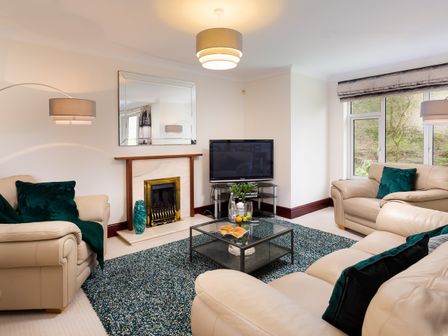 A living room with beige sofas green cushions a glass coffee table a fireplace and a television at Beech View in Ambleside