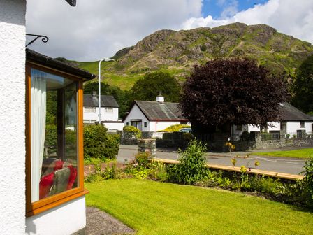 A garden with a lawn and plants in front of houses with a mountain in the background at Sethera in Coniston