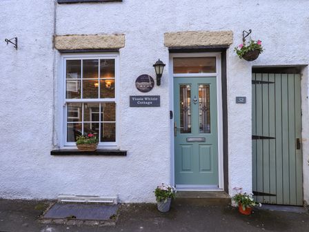 A white cottage exterior with a blue door and window with flower pots at Tizzie Whizie Cottage in Windermere