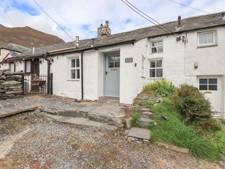 The exterior of a white cottage with a stone pathway and stairs at Blease Garth in Threlkeld