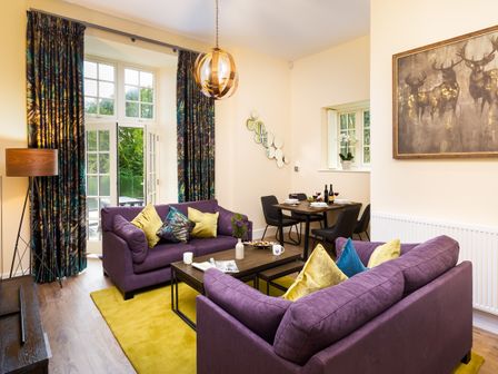 A living room with two purple sofas and yellow pillows a wooden coffee table yellow rug and dining table at Larna Place Ambleside