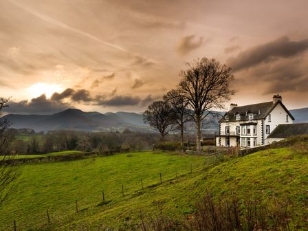 A house with trees beside a green field and mountains in the background at One The Howe in keswick