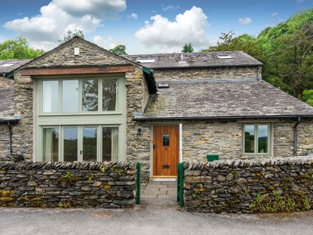 Stone cottage with large windows wooden door and stone wall with metal gate at Cragfell Cottage Cartmel Fell