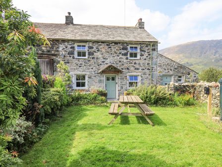 A stone cottage with four windows and a door with a picnic table on a lawn in front at Yew Tree Cottage Borrowdale
