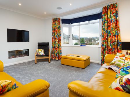A living room with yellow leather sofas and colorful curtains at Fell View in Keswick