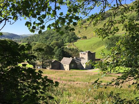 A countryside view with stone buildings in a green valley surrounded by trees at Kentmere Hall Bank Barn in Kentmere