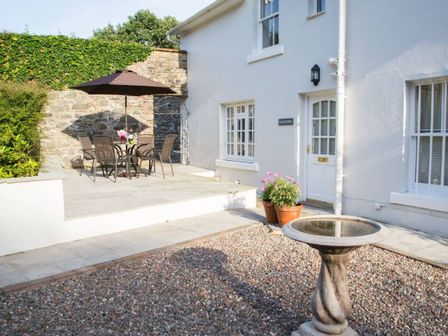 An outdoor patio area with a table and chairs under an umbrella a birdbath and flower pots outside a white house at Scots Pine in Keswick